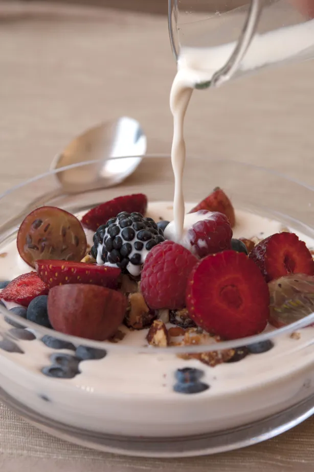 Sahne wird über eine Schüssel mit gemischten Beeren und Granola gegossen, Nahaufnahme eines Frühstücksgerichts