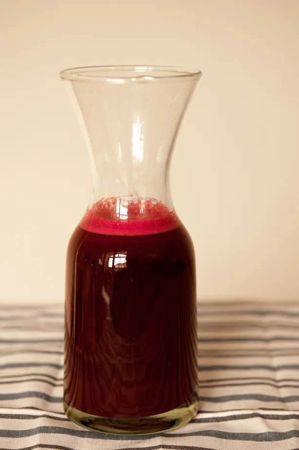Glaskaraffe mit tiefrotem Saft auf gestreiftem Stoff, kräftige Beerentöne