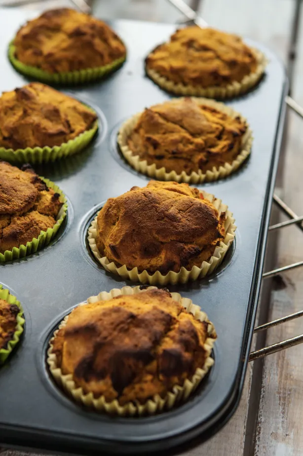 Frisch gebackene Muffins in Papierförmchen auf dunklem Backblech, goldbraune heimische Stimmung
