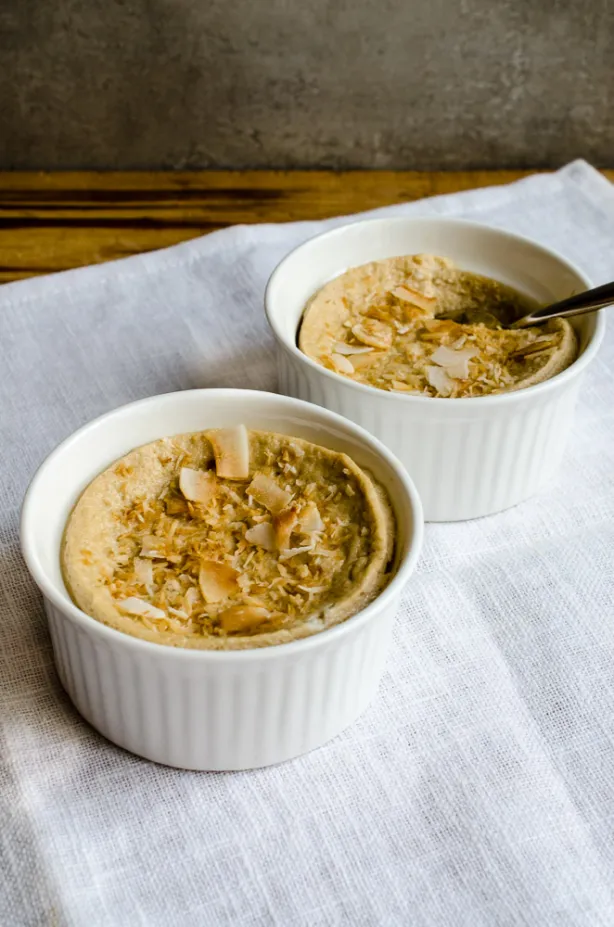 Zwei weiße Förmchen mit gebackenem Pudding, bestreut mit geröstetem Kokosflocken, auf weißem Tuch